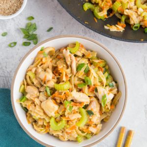 Skillet with Asian noodles inside and a bowl of Asian noodles with chopsticks and green onions to the side.