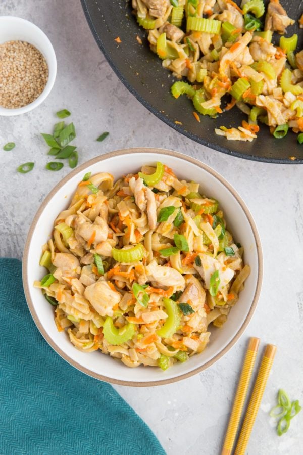 Skillet with Asian noodles inside and a bowl of Asian noodles with chopsticks and green onions to the side.