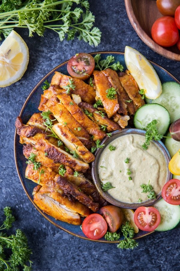 Plate of chicken shawarma with sauce and fresh vegetables to the side.