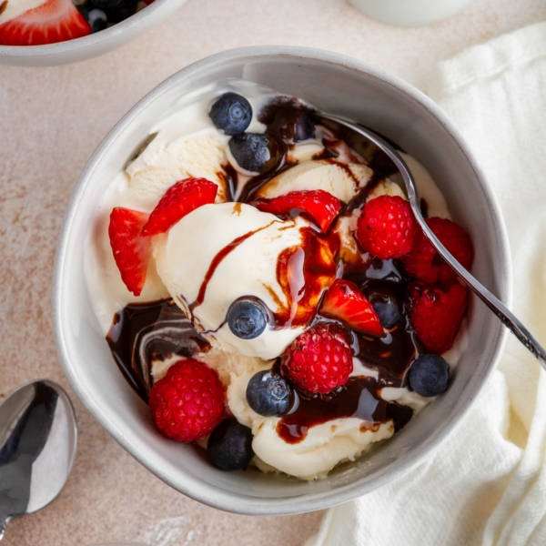 Homemade vanilla ice cream in a bowl with fresh berries and chocolate sauce, ready to eat