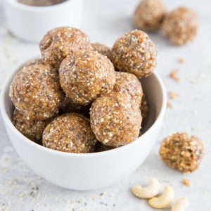 Large white bowl of energy balls with raw nuts and seeds sprinkled around, ready to eat