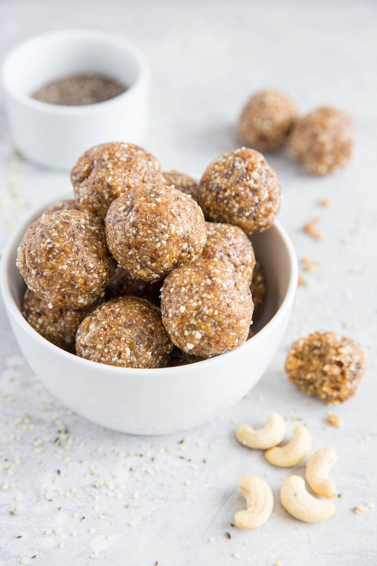 Large white bowl of energy balls with raw nuts and seeds sprinkled around, ready to eat