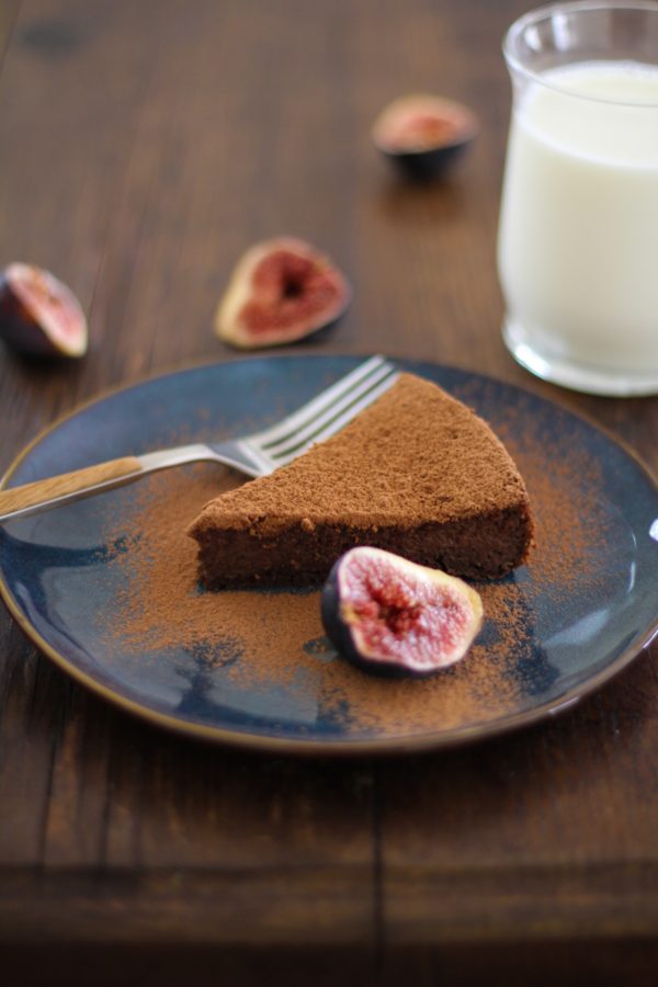 Slice of chocolate cake on a blue plate with a roasted fig to the side.