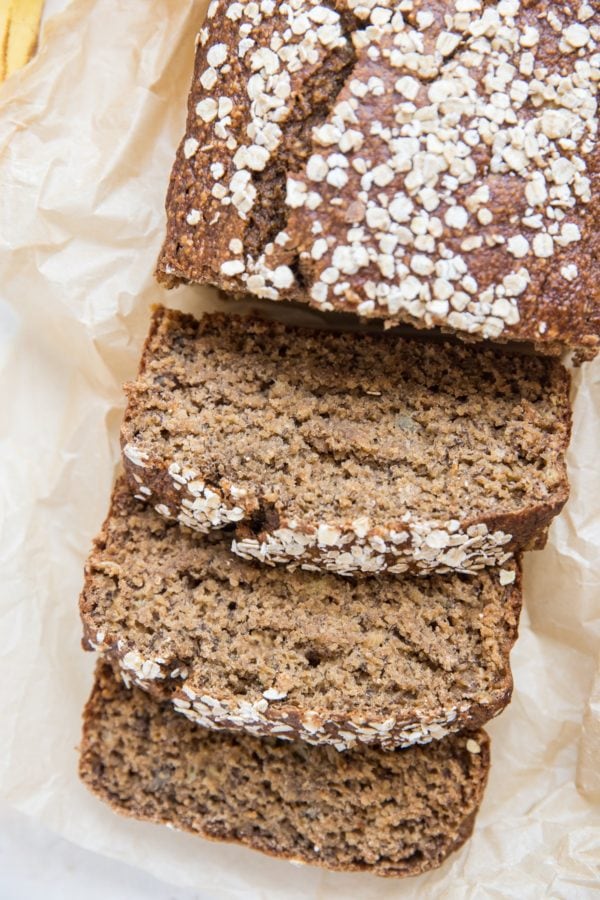 Loaf of gluten-free oatmeal banana bread cut into slices on a sheet of parchment paper.