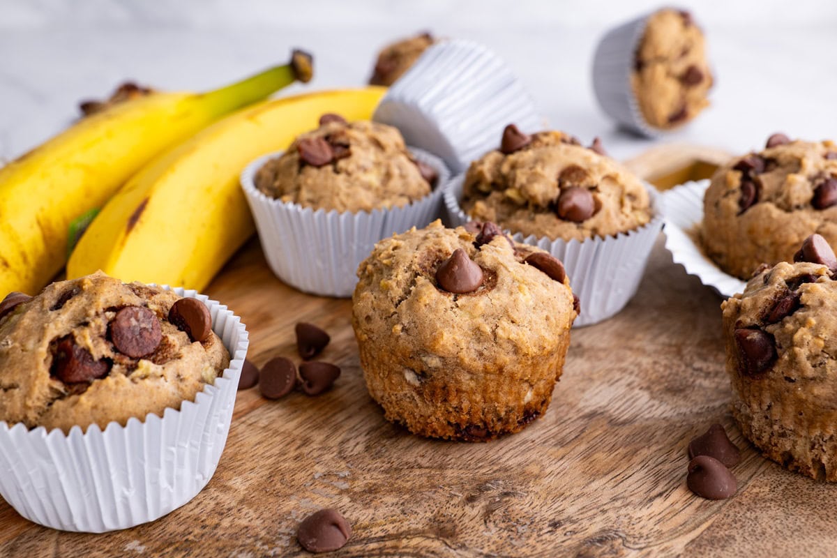 Gluten-free banana muffins on a wooden cutting board with fresh bananas in the background.