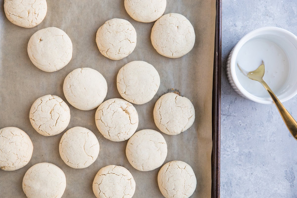 Baking sheet with sugar cookies fresh out of the oven and a powdered sugar glaze to the side, ready to frost.