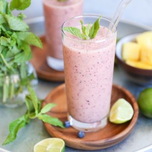 Two fruit smoothies in glasses in a serving tray with fresh fruit