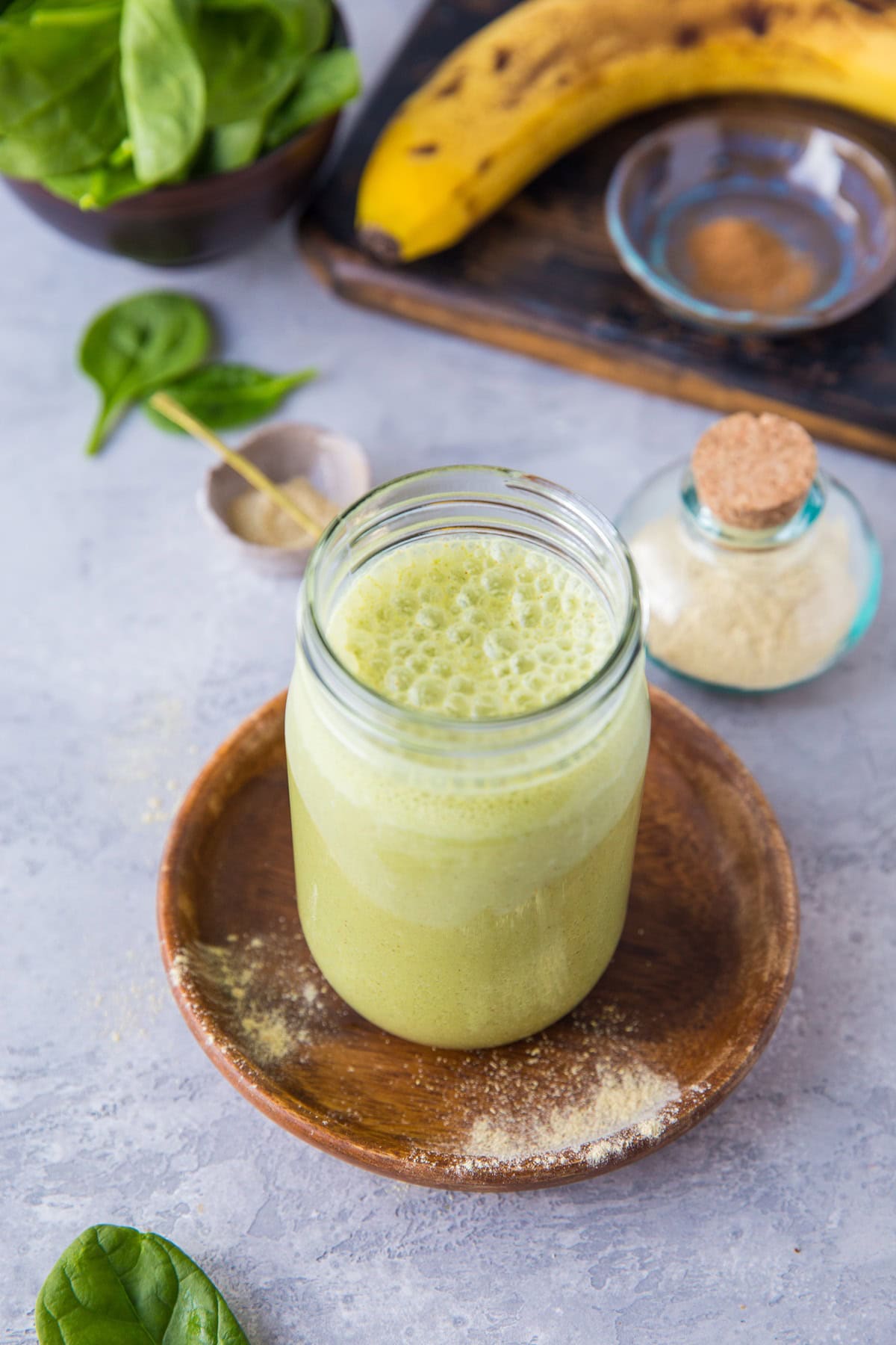 Green smoothie in a jar with fresh spinach and a ripe banana in the shot.