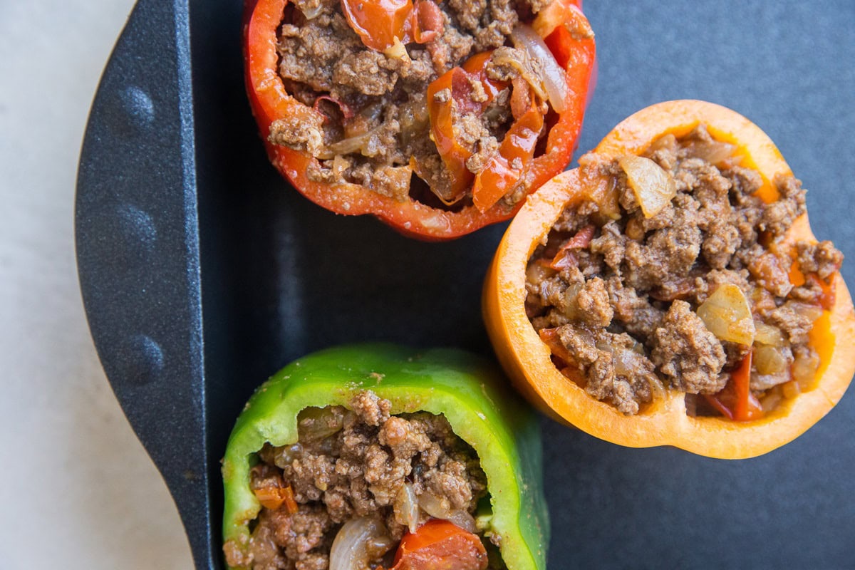 Casserole dish with raw peppers stuffed with ground meat mixture, ready to go into the oven.