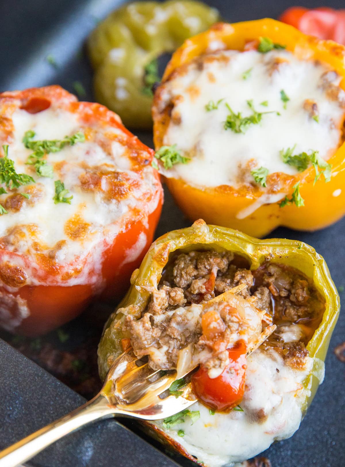 Baking dish full of bell peppers with a fork pulling cheese off of a stuffed pepper.