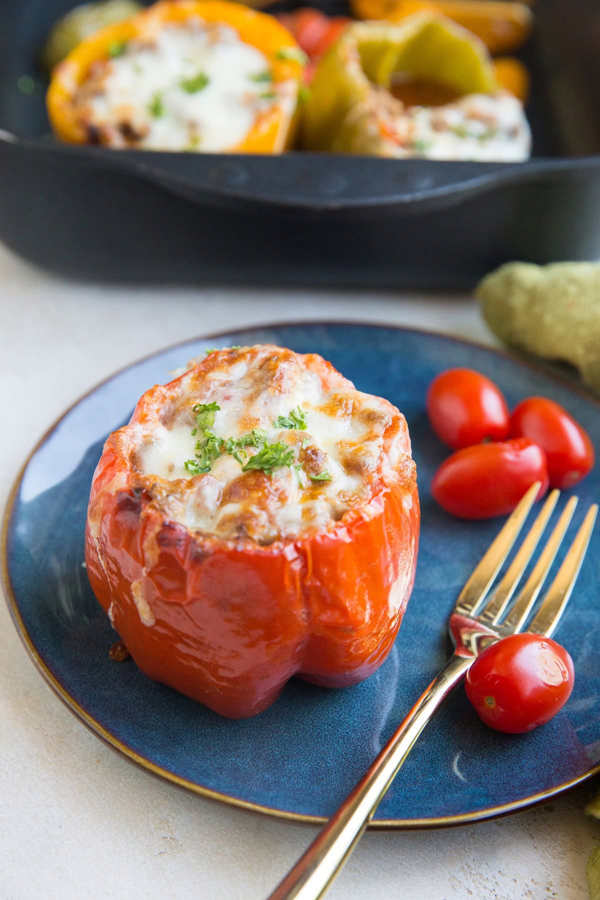 Blue plate with a stuffed bell pepper on top with a gold fork for eating and the rest of the stuffed peppers in a baking tray in the background.