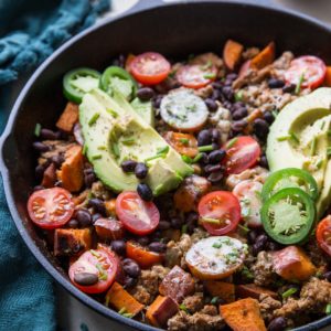 Cast iron skillet full of ground turkey, sweet potatoes, black beans, avocado, and more.