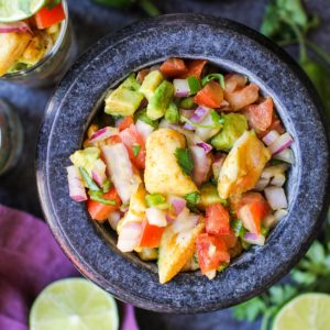 Large black bowl of fresh fish ceviche with fresh limes and cilantro around the bowl and a purple napkin.