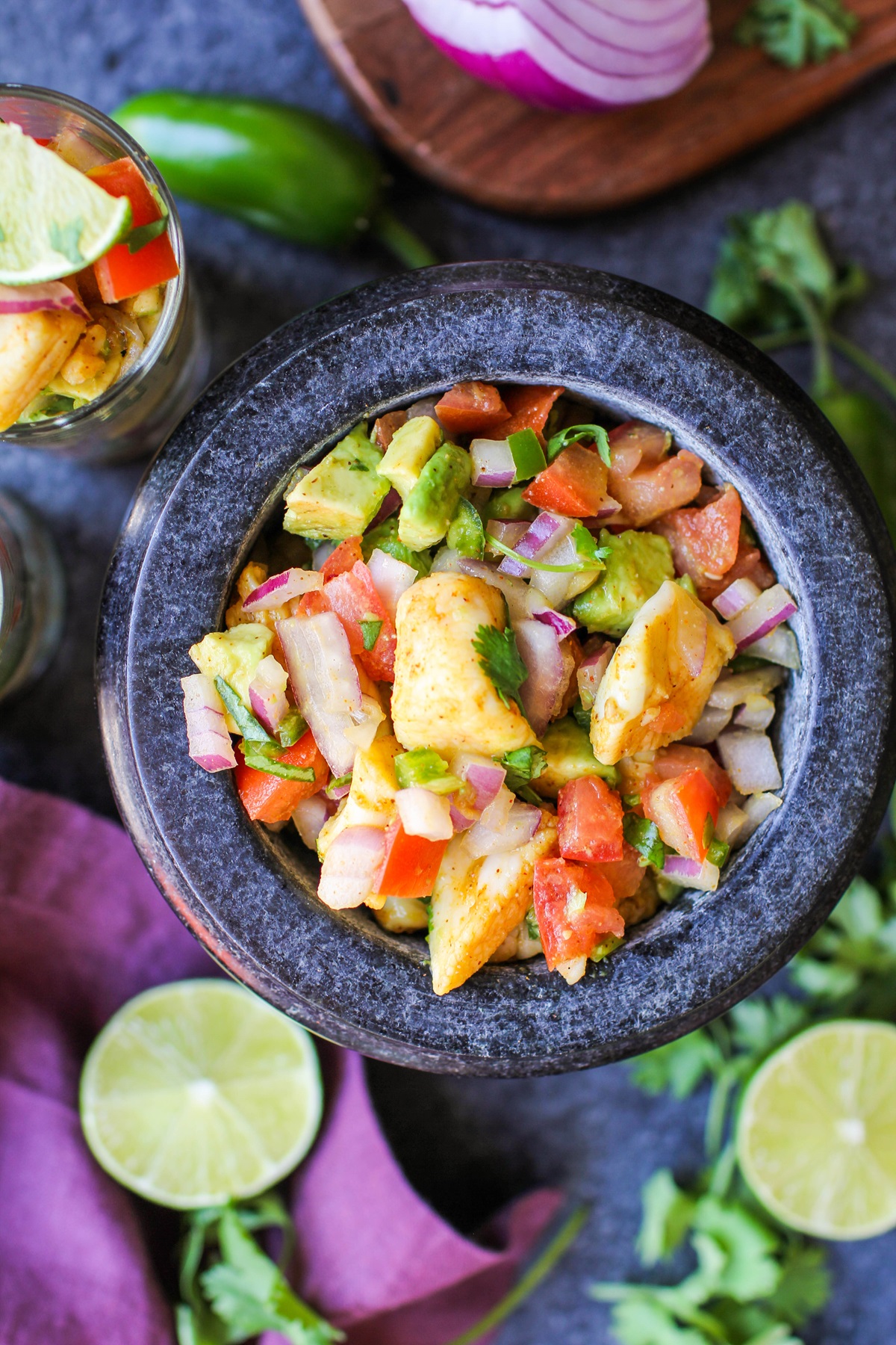 Large black bowl of fresh fish ceviche with fresh limes and cilantro around the bowl and a purple napkin.