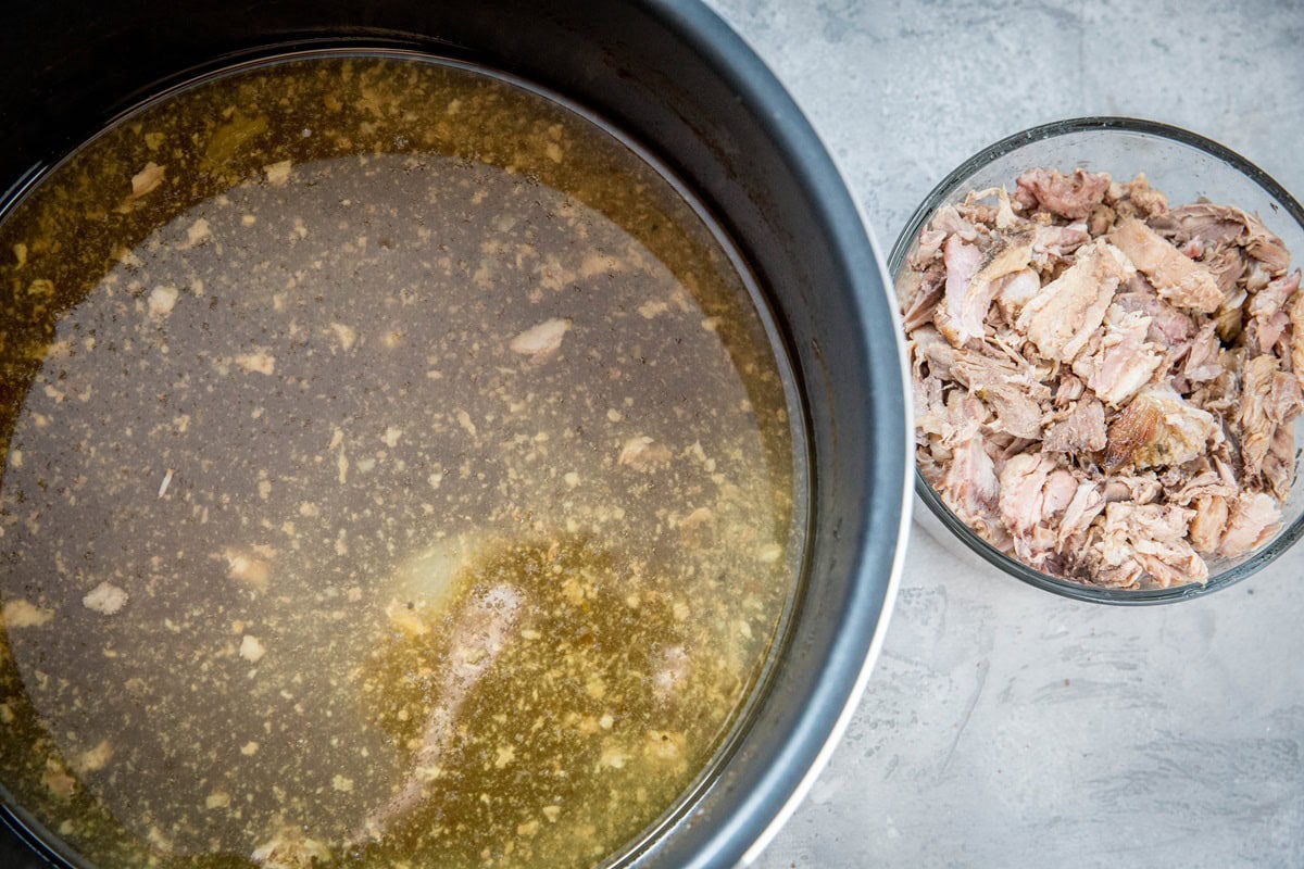 Instant pot full of broth with bits of turkey pieces inside and a bowl full of turkey meat to the side.