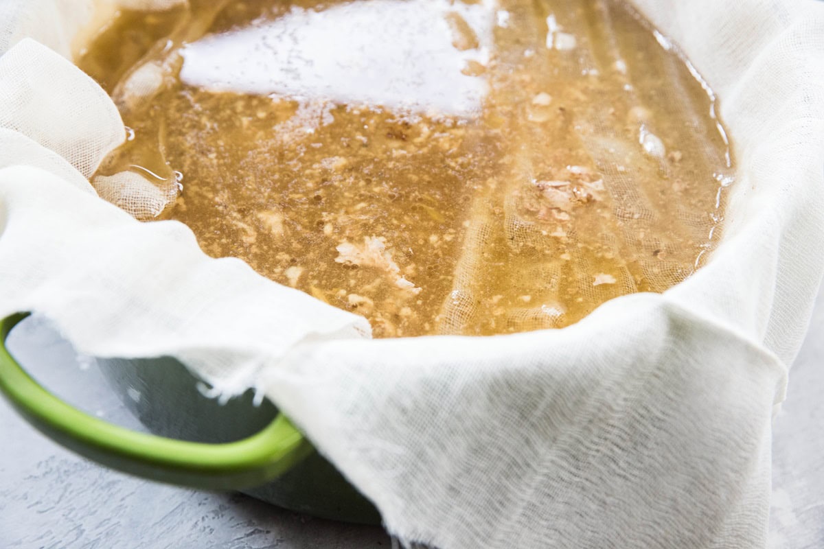 Pot with cheesecloth and bone broth being filtered through the cloth.