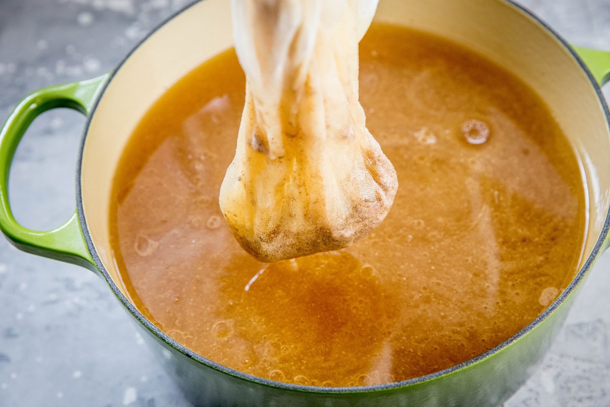 Large pot with cheesecloth scooping solids out of bone broth.