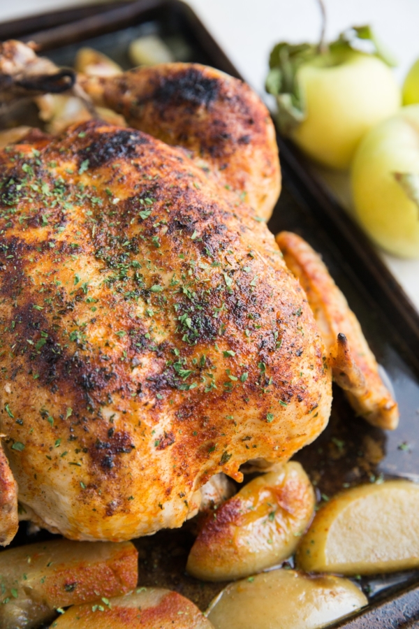 Whole juicy chicken sitting on a large baking sheet with cooked apples all around. Ready to serve with side dishes.