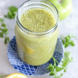 glass of liver detox smoothie with fresh lemon and parsley to the side.