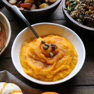 Big white bowl full of mashed kabocha squash with side dishes all around on a holiday table.