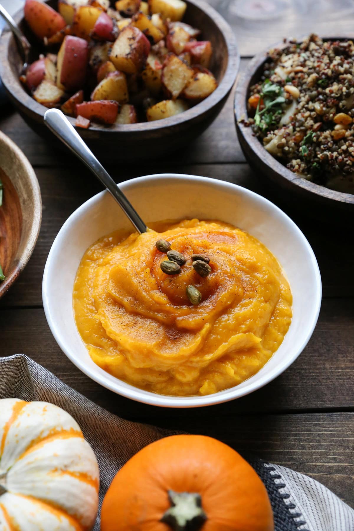 Big white bowl full of mashed kabocha squash with side dishes all around on a holiday table.