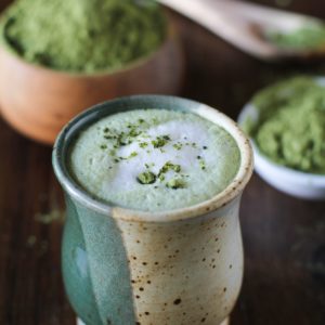 Matcha Green Tea Latte in a fancy ceramic mug with a pile of matcha in the background.