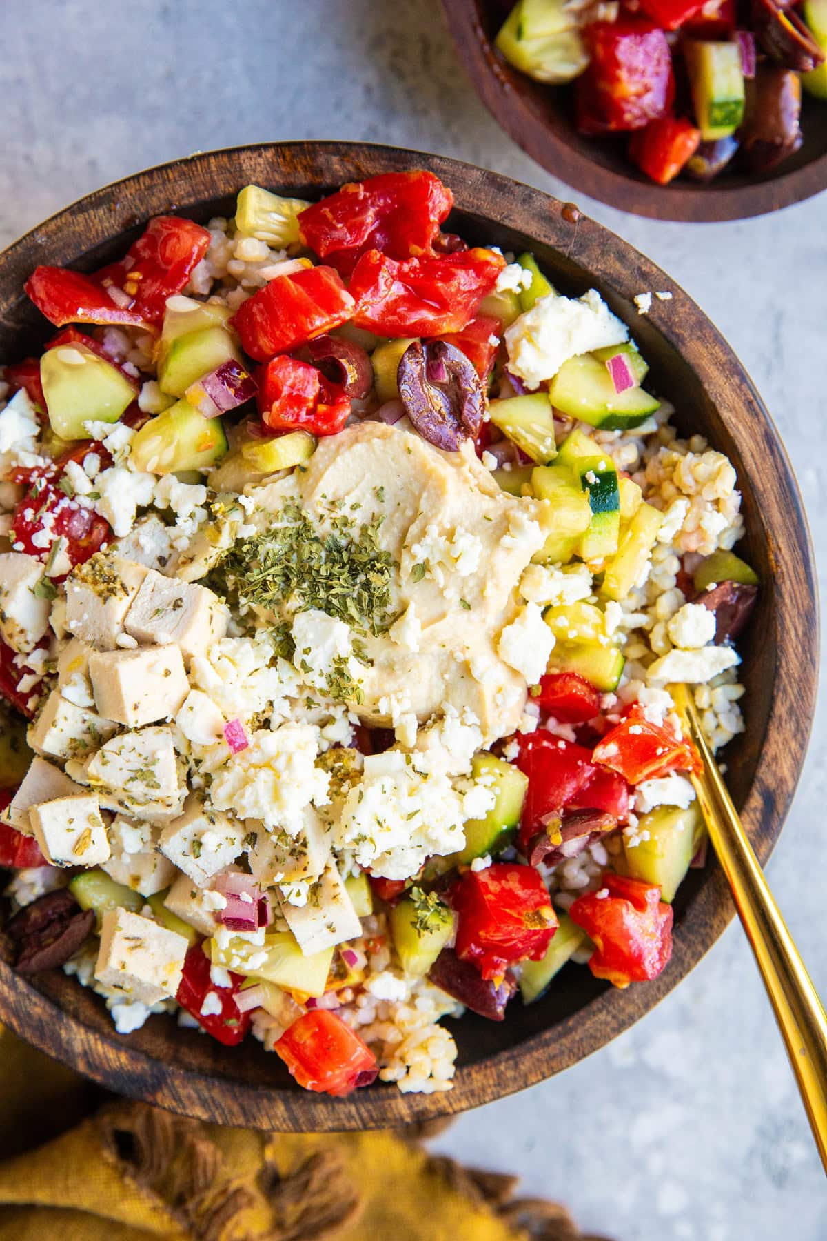 Big wooden bowl of chicken, hummus, rice, and cucumber tomato salad.