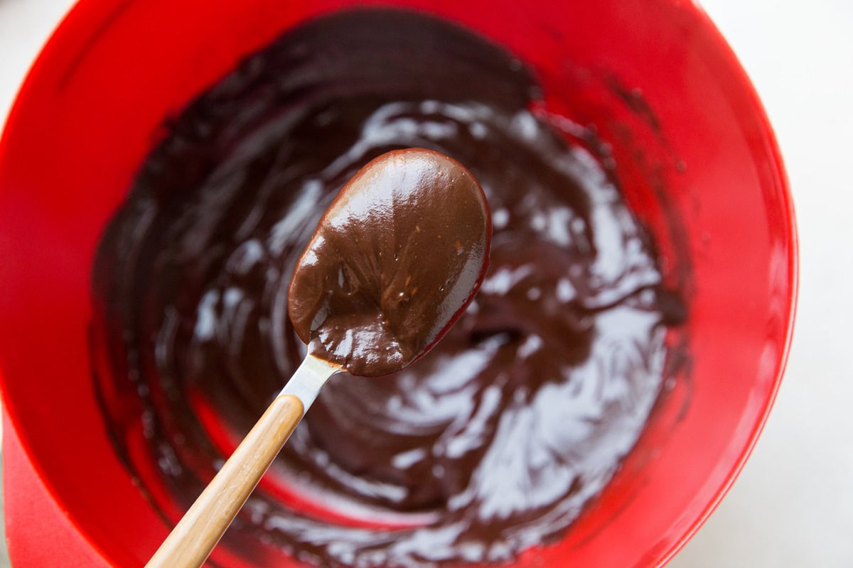 Spoonful of chocolate ganache over a mixing bowl, ready to be used.