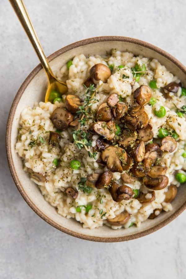 Large ceramic bowl full of creamy rice with sauteed mushrooms on top, ready to serve.