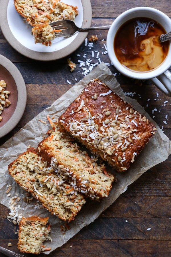 Loaf of morning glory muffin bread on a wooden background, cut into thick slices with a mug of coffee to the side.