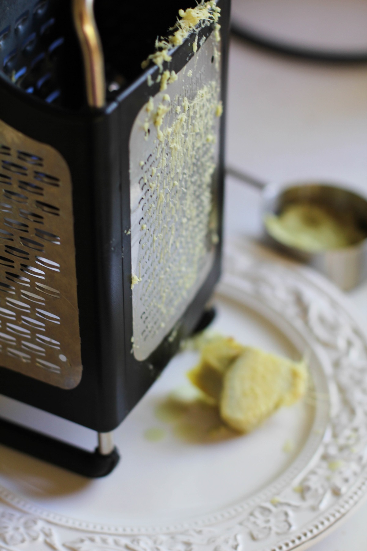 Box grater on a plate with fresh ginger grated on it