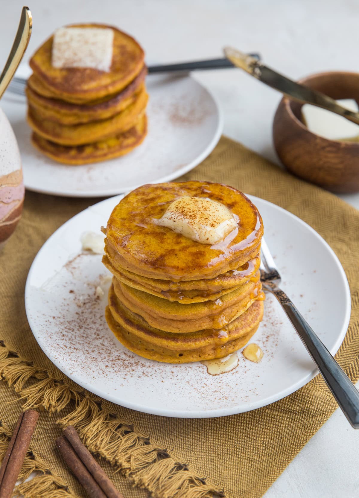 two plates of pumpkin pancakes with butter and syrup, ready to serve