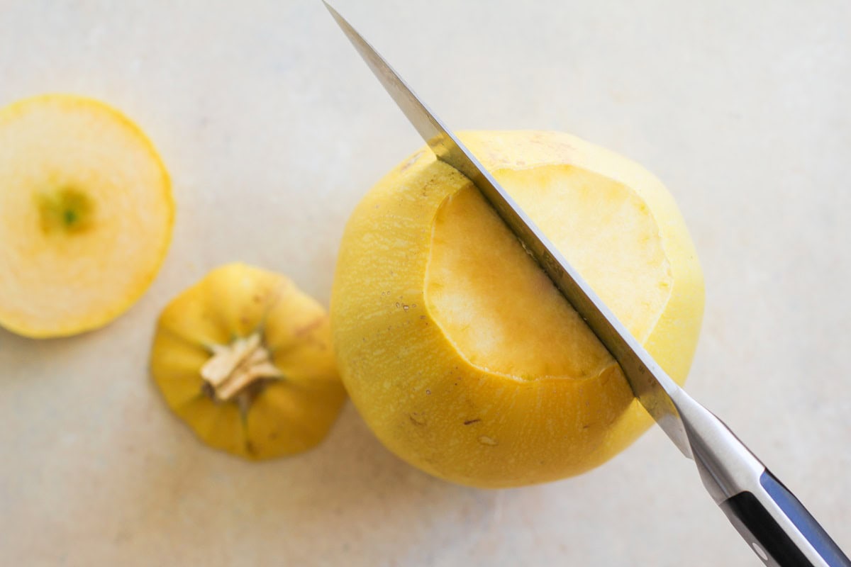 Chef's knife cutting into a spaghetti squash down the center lengthwise.