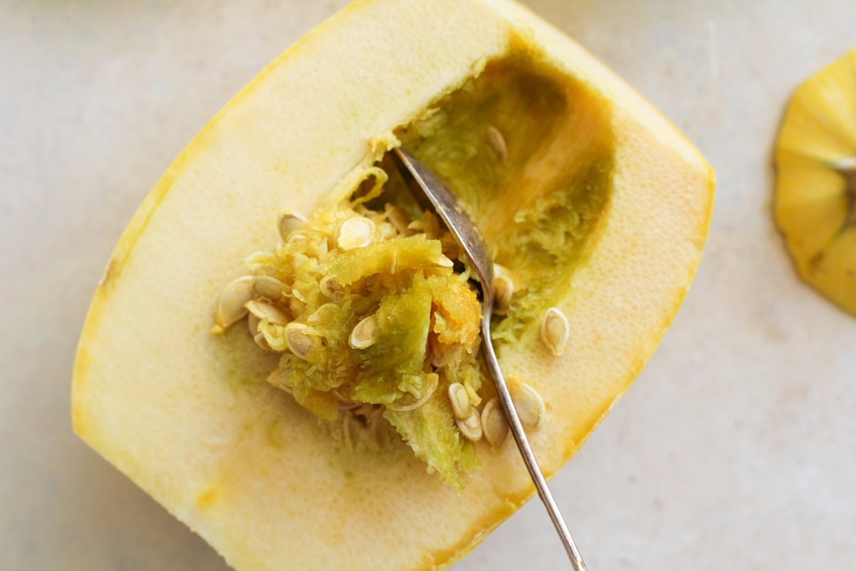 Spoon scooping the seeds out of a spaghetti squash.