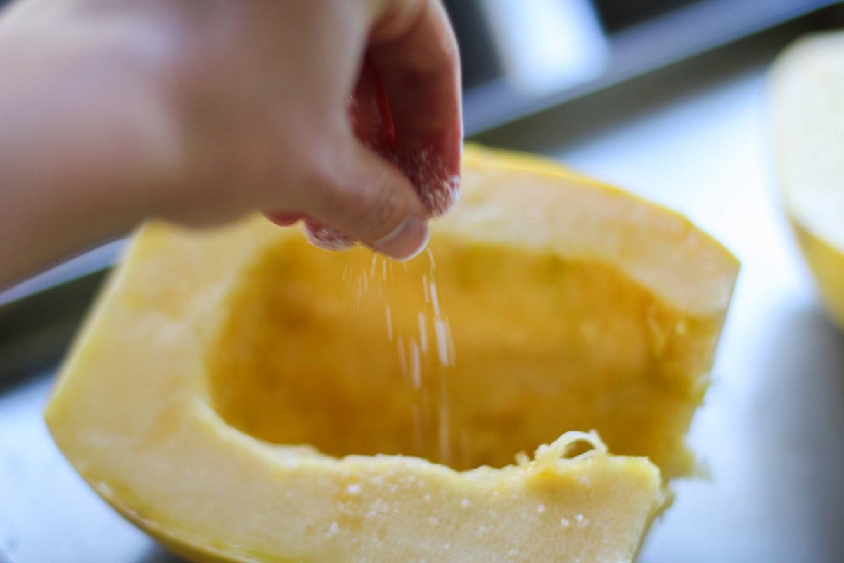 Hand sprinkling the flesh of a spaghetti squash with salt.