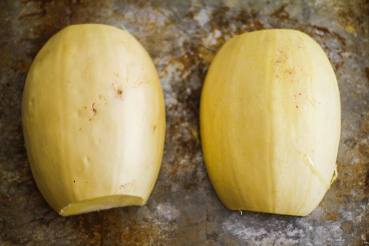 Two spaghetti squash halves on a baking sheet, ready to go into the oven.