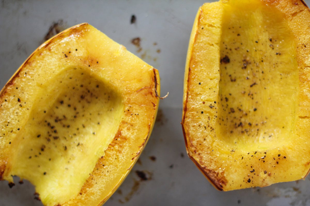 Two spaghetti squash halves cut side up on a roasting pan, finished roasting and ready to eat.