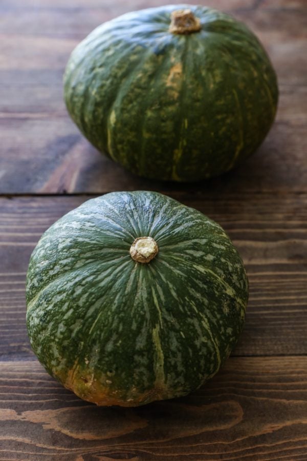 Two green kabocha squash on a wooden table.