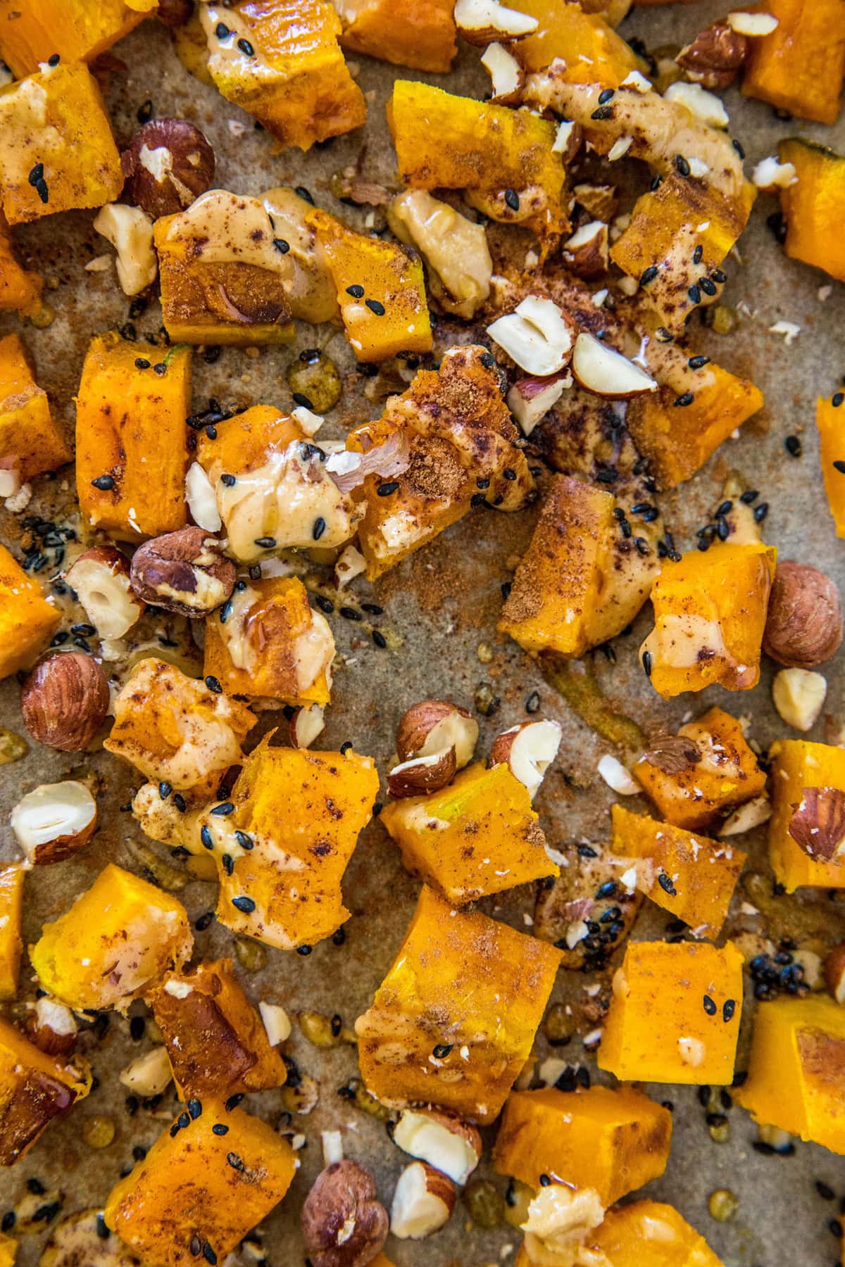 Close up photo of roasted kabocha squash on a baking sheet with tahini and hazelnuts 