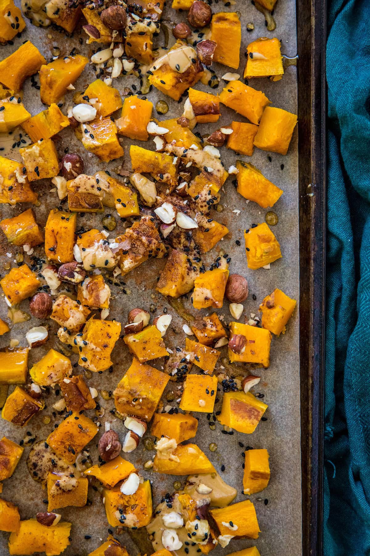 Sheet pan full of chopped roasted kabocha squash sprinkled with nuts and drizzled with a sauce.