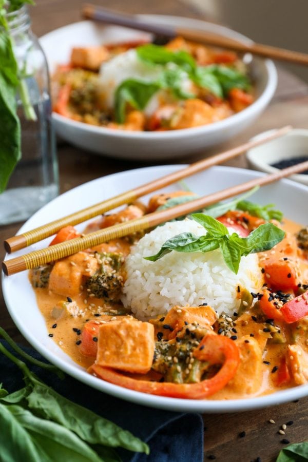 Two bowls of salmon curry with scoops of rice in the center and fresh basil all around. Chop sticks and a blue napkin for serving.