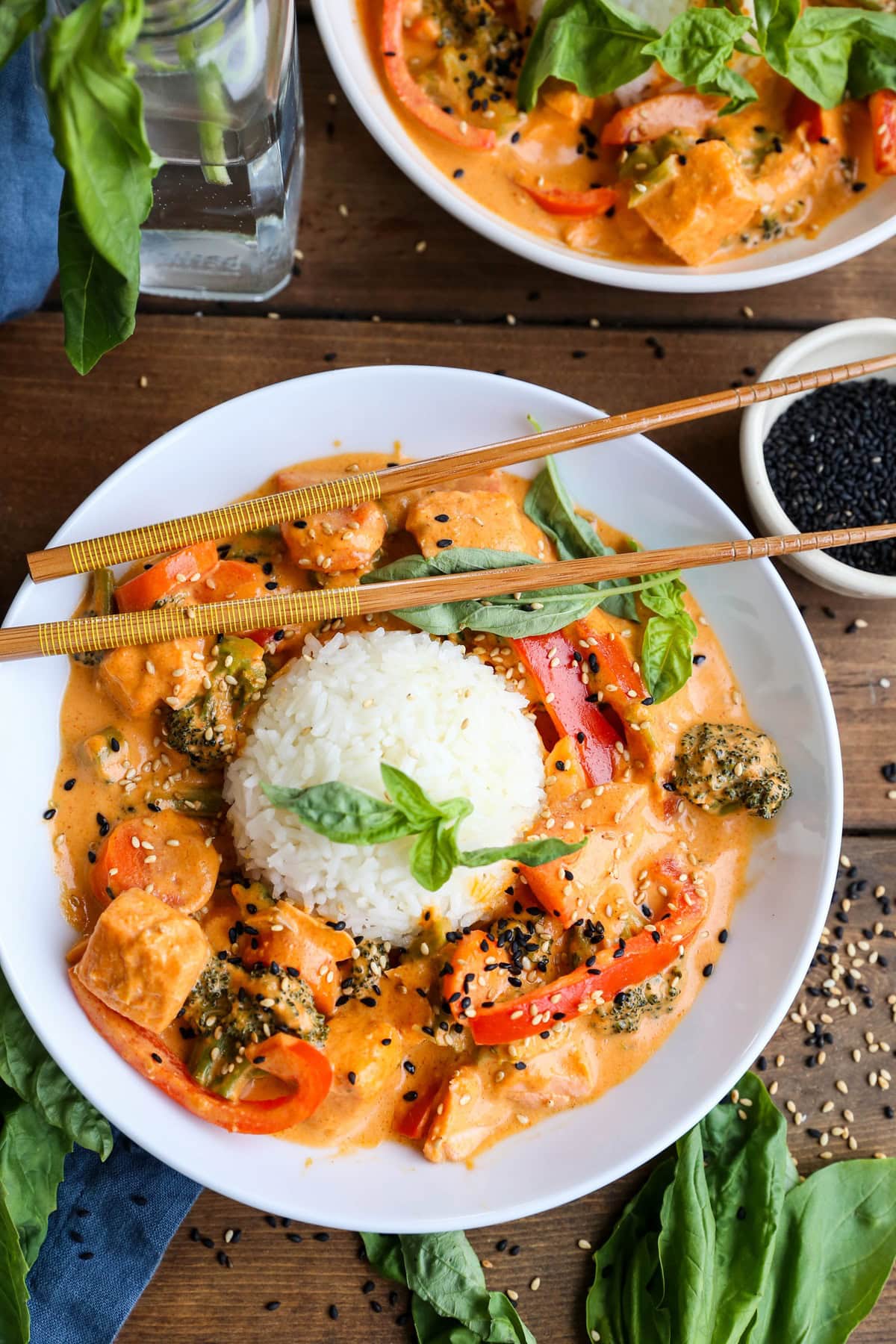 Two white bowls full of salmon curry with scoops of white rice in the center. Sprinkles of sesame seeds all around.