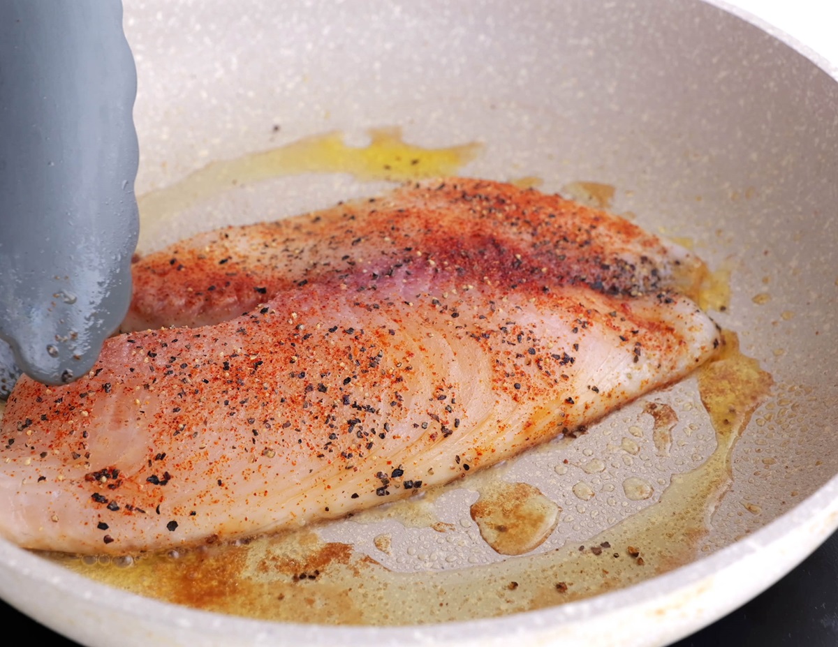 White fish cooking in a skillet in oil.
