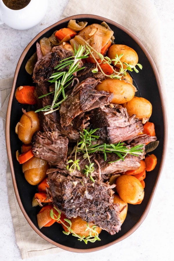 Platter of shredded beef on top of potatoes, carrots, and onions, ready to serve.