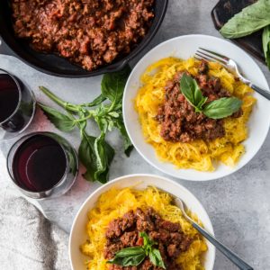 Two white bowls of spaghetti squash with red sauce on top and fresh basil leaves and a napkin to the side.