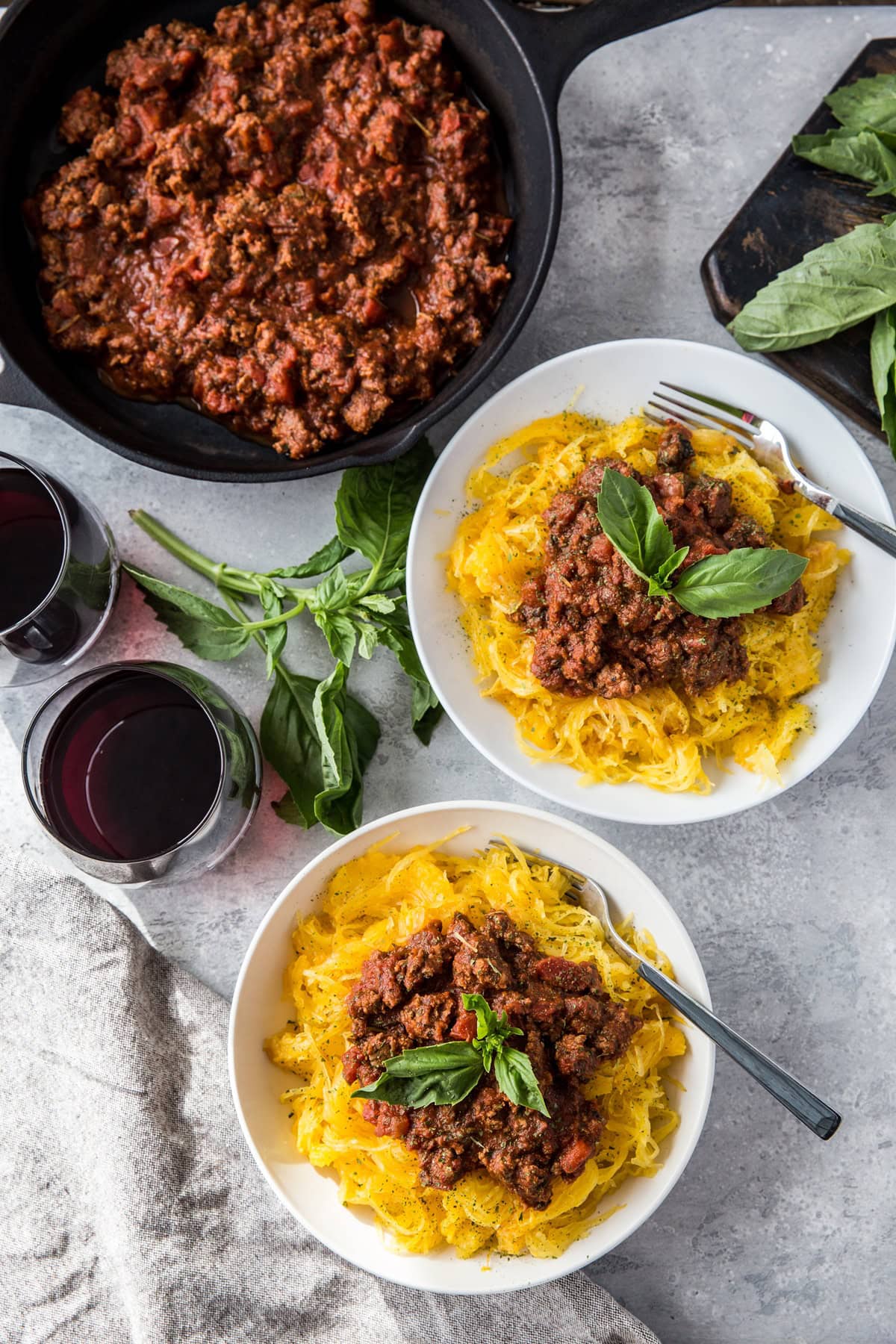 Two white bowls of spaghetti squash with red sauce on top and fresh basil leaves and a napkin to the side.