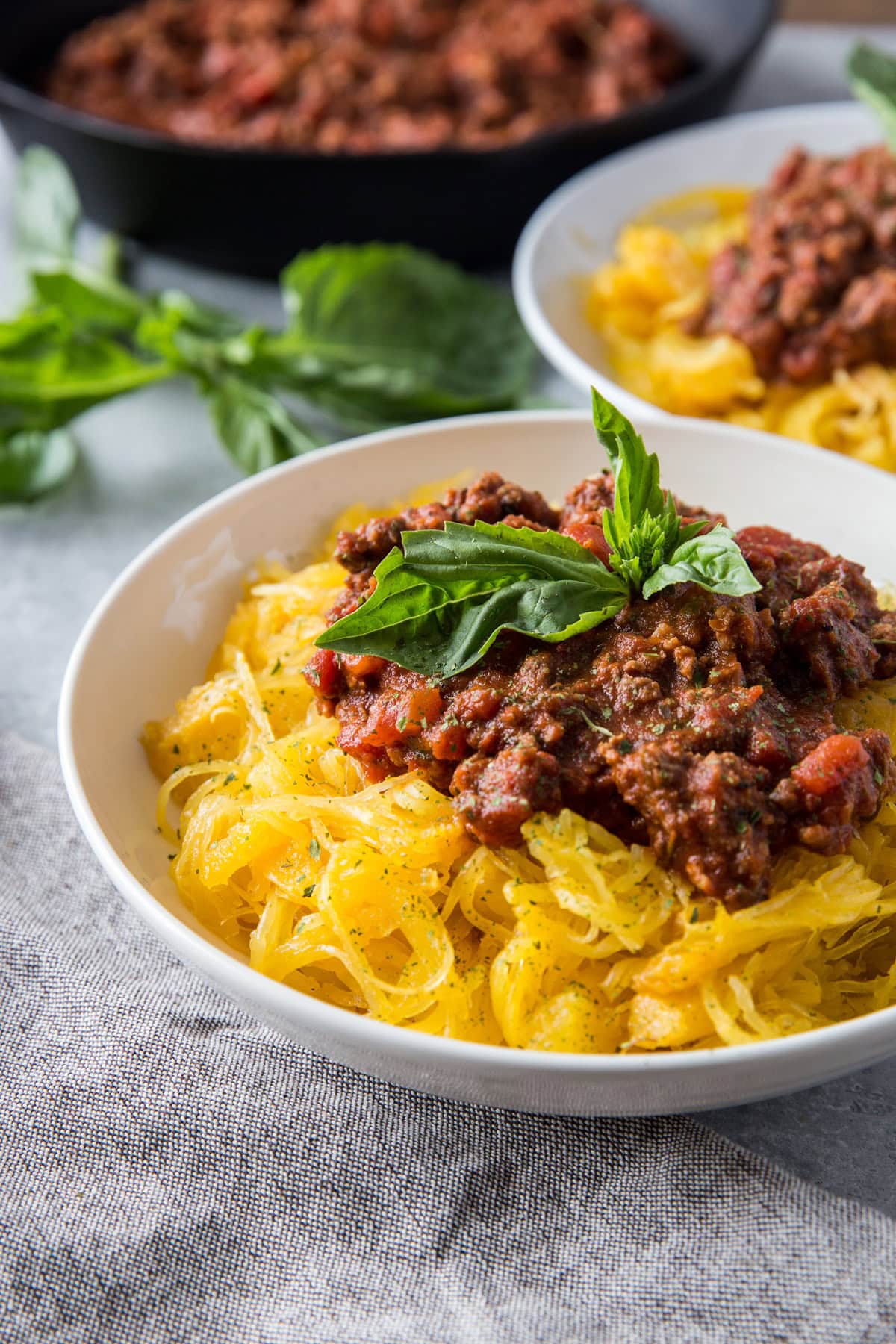 Big white bowl of spaghetti squash with red meat sauce on top and a basil leaf.