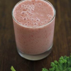 Glass of strawberry banana smoothie with a kale leaf to the side.