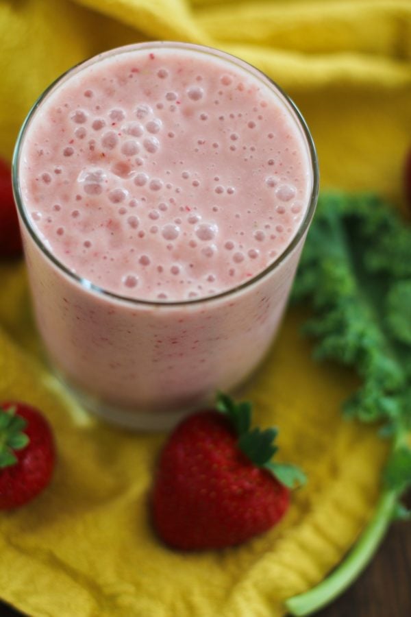 Glass of strawberry banana smoothie with a kale leaf to the side.