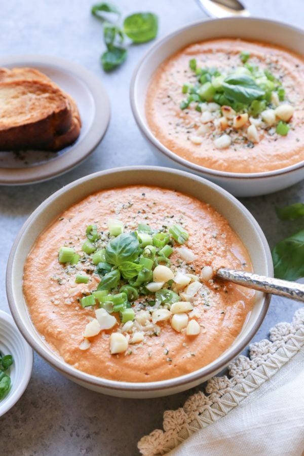 Creamy Vegan Tomato Basil Soup in two bowls with fresh basil on top and a cream colored napkin to the side.